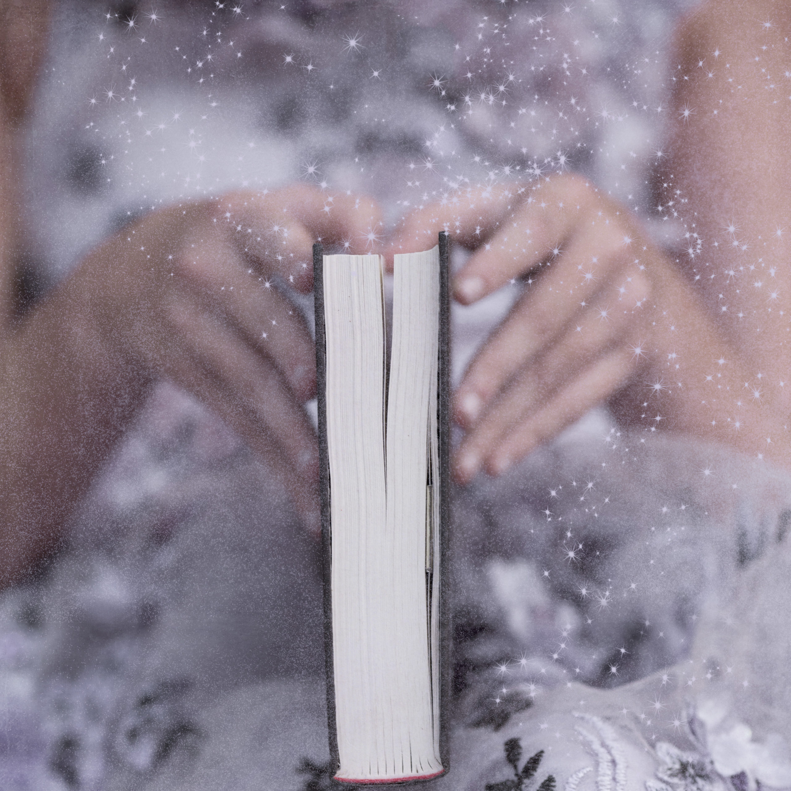 Photo of a girl's hands holding a closed book with magical sparkles all around. The girl is wearing a violet colored dress by Anna Triant Couture.